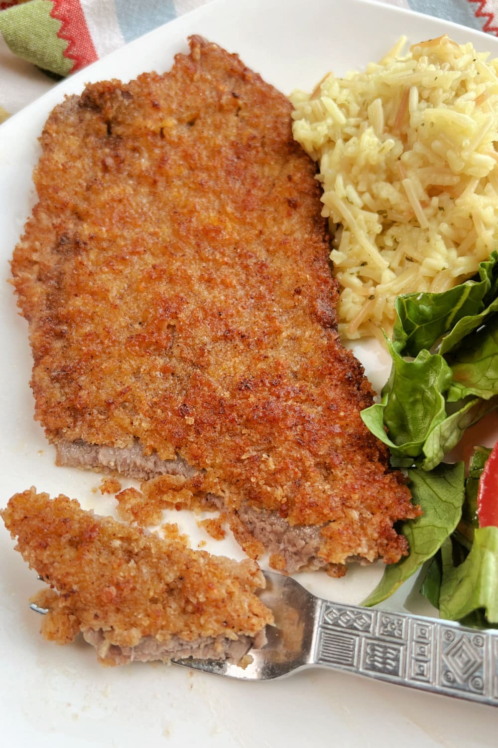 A bite of Milanesa Steak on a fork, resting on a white plate. 