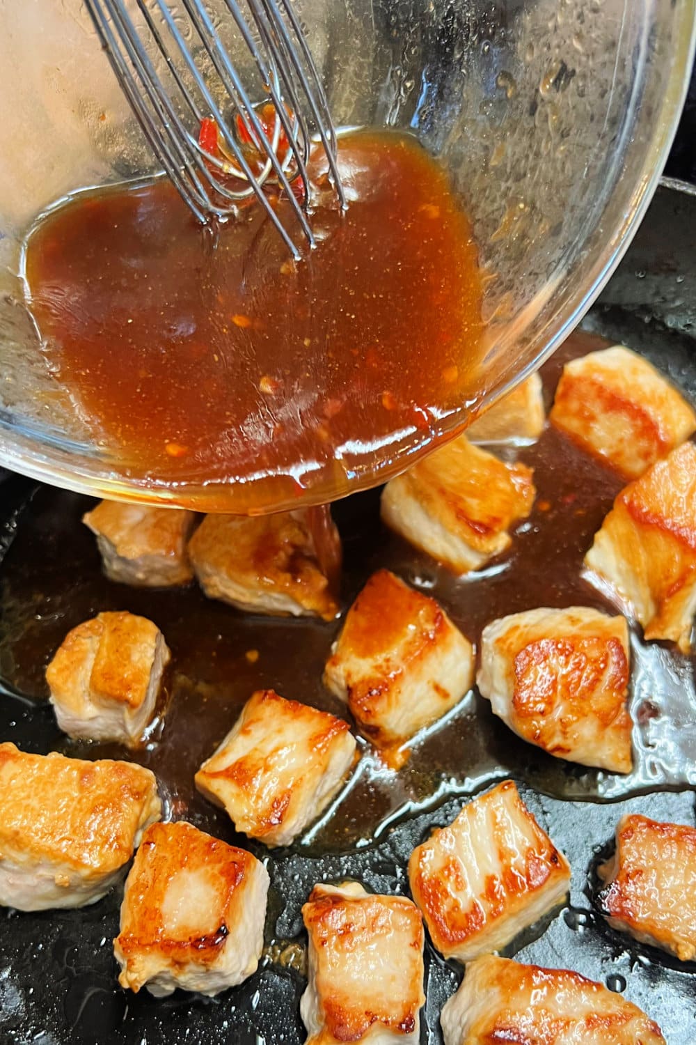 Sauce being poured into pan with pork cubes. 