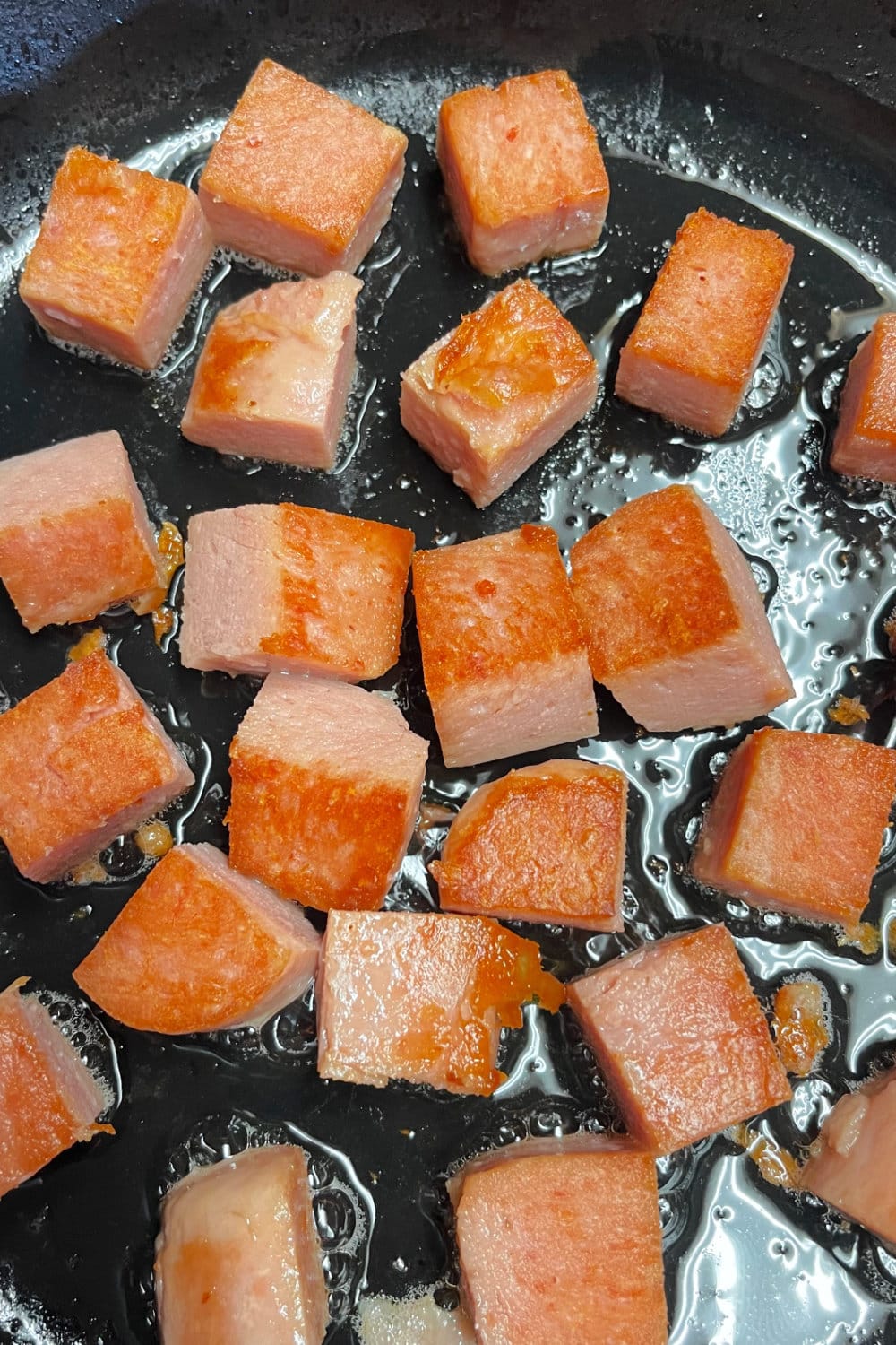 Cubes of Spam that have been browned in hot oil in a skillet. 