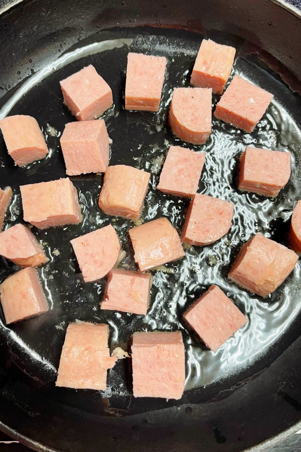 Cubes of Spam added to a skillet of hot oil. 