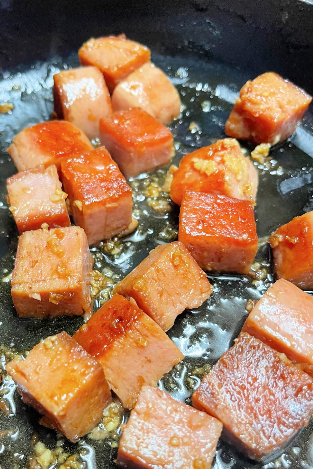 Golden brown Spam simmering in sauce ingredients. 