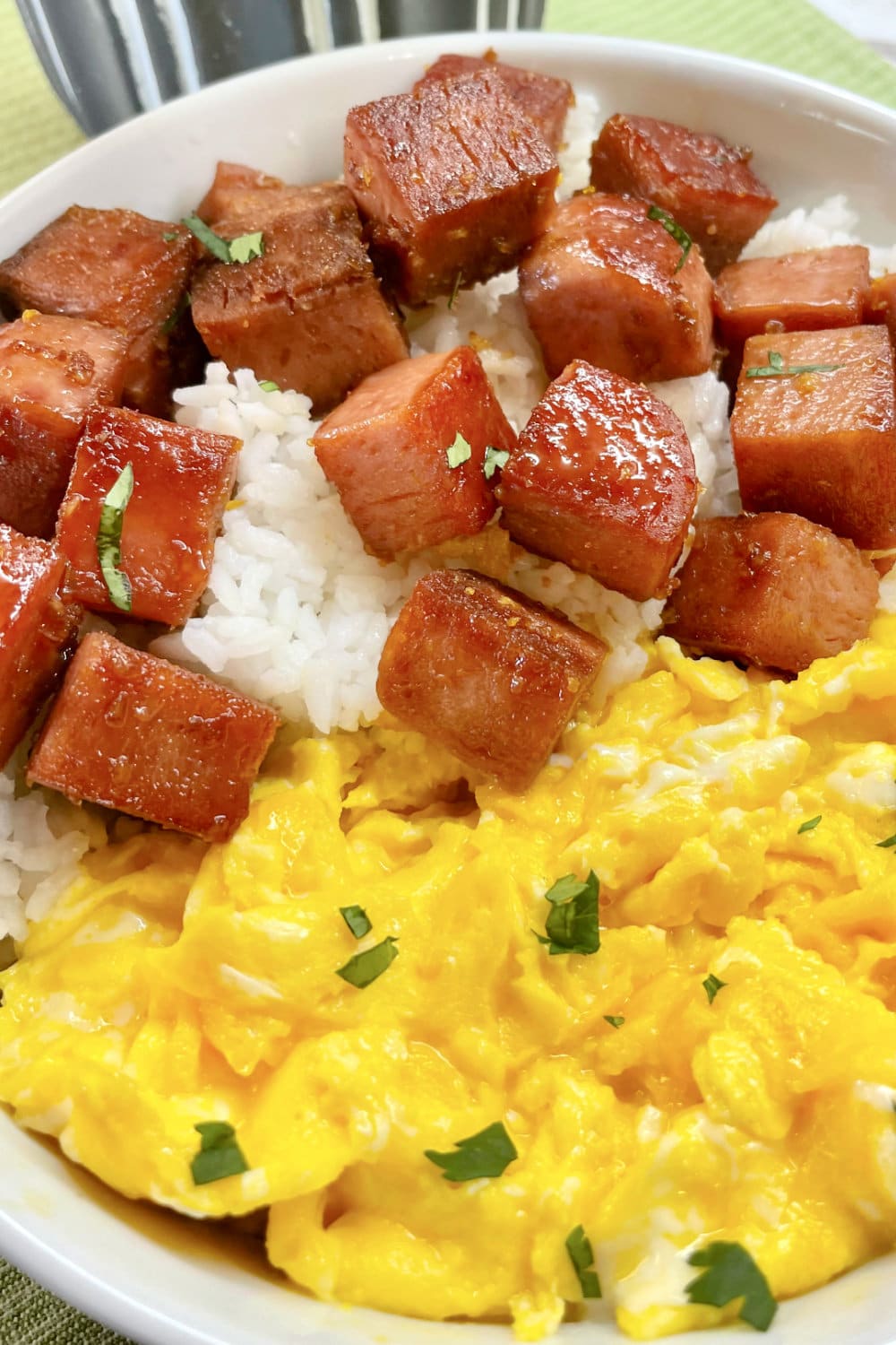 Spam over Rice in a white bowl with scrambled eggs. 