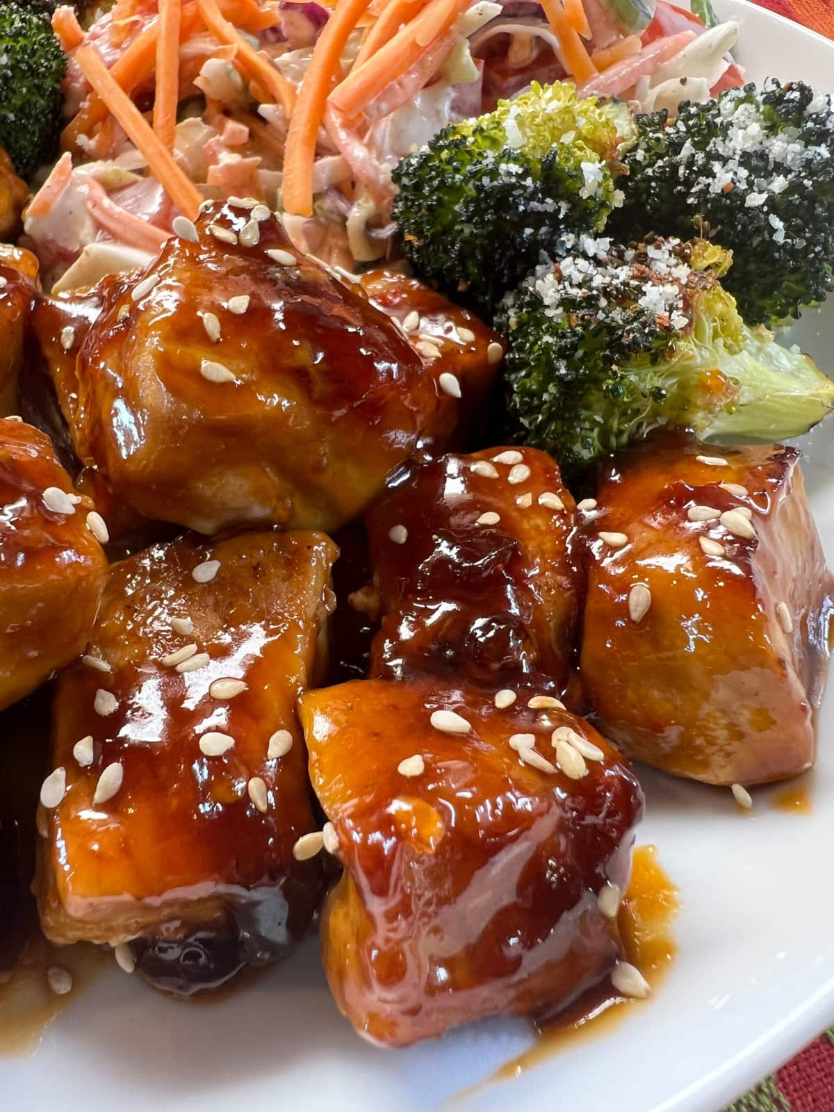 Saucy pork cubes with broccoli and salad on a white plate. 