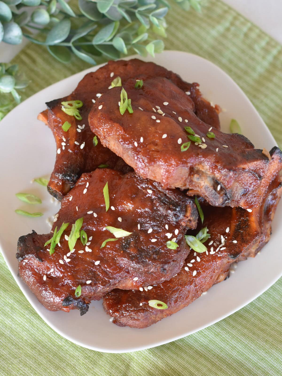 country-style-ribs-asian-plated Country Style Ribs with Asian BBQ Sauce stacked on top of each other on a white plate with seasame seeds and green onions.