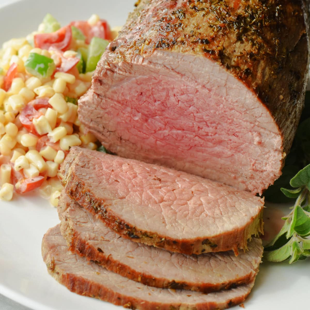 A sliced medium-rare eye of round roast on a white platter.