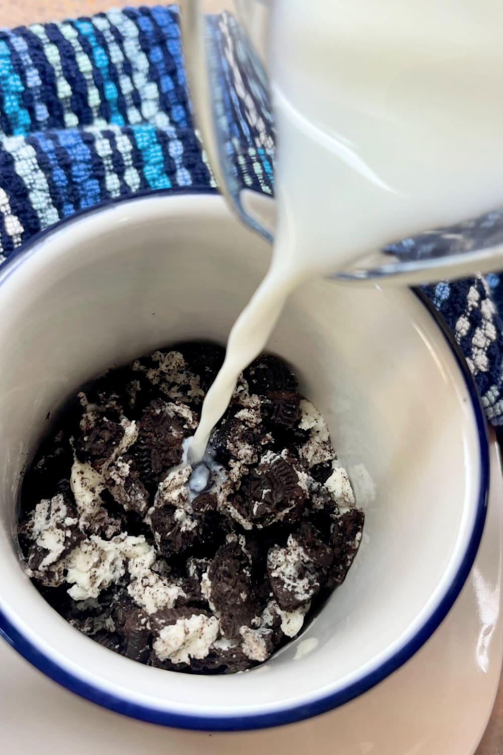 Milk poured over crushed Oreo cookies in a mug.