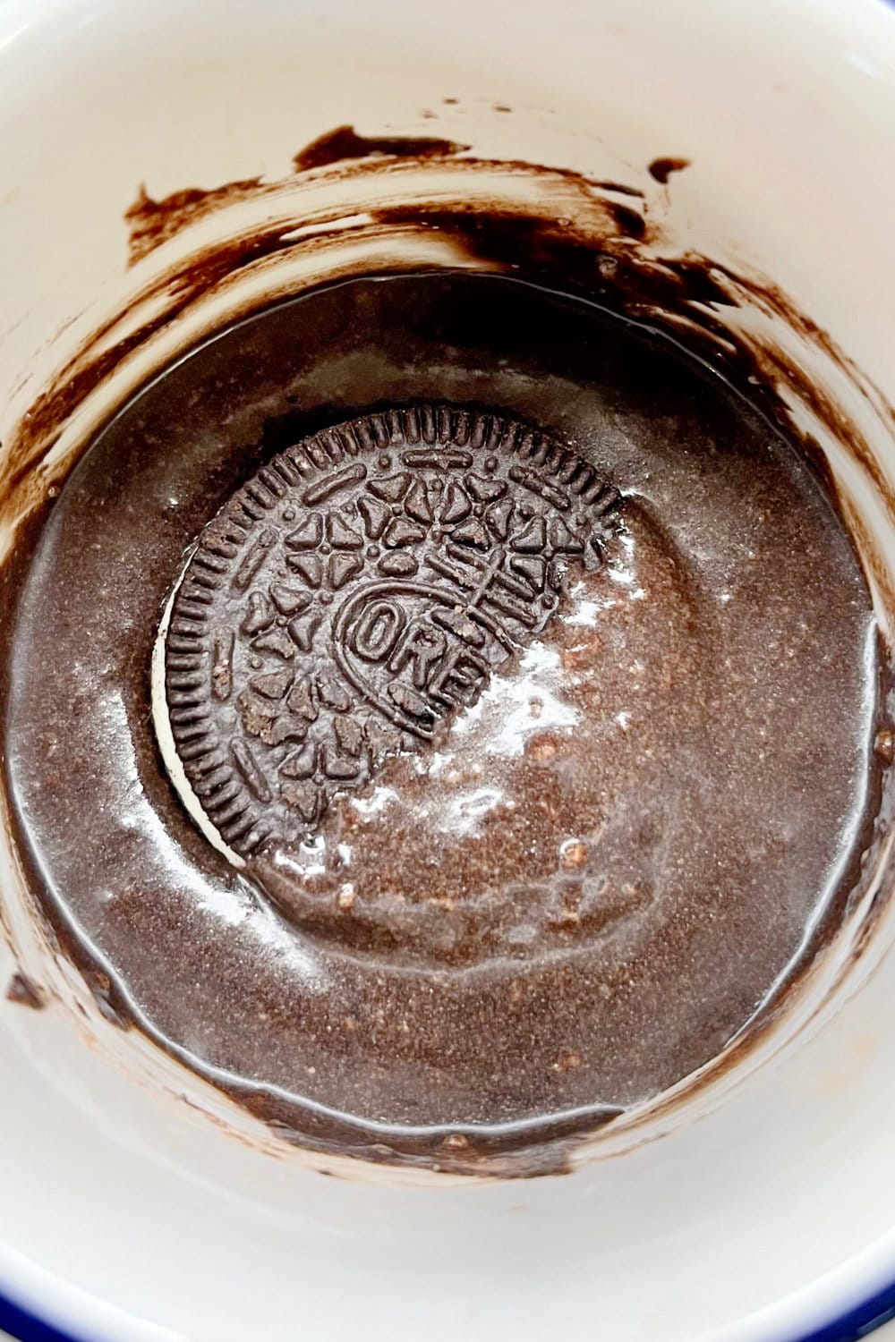 An Oreo cookie pressed down into mug cake batter. 