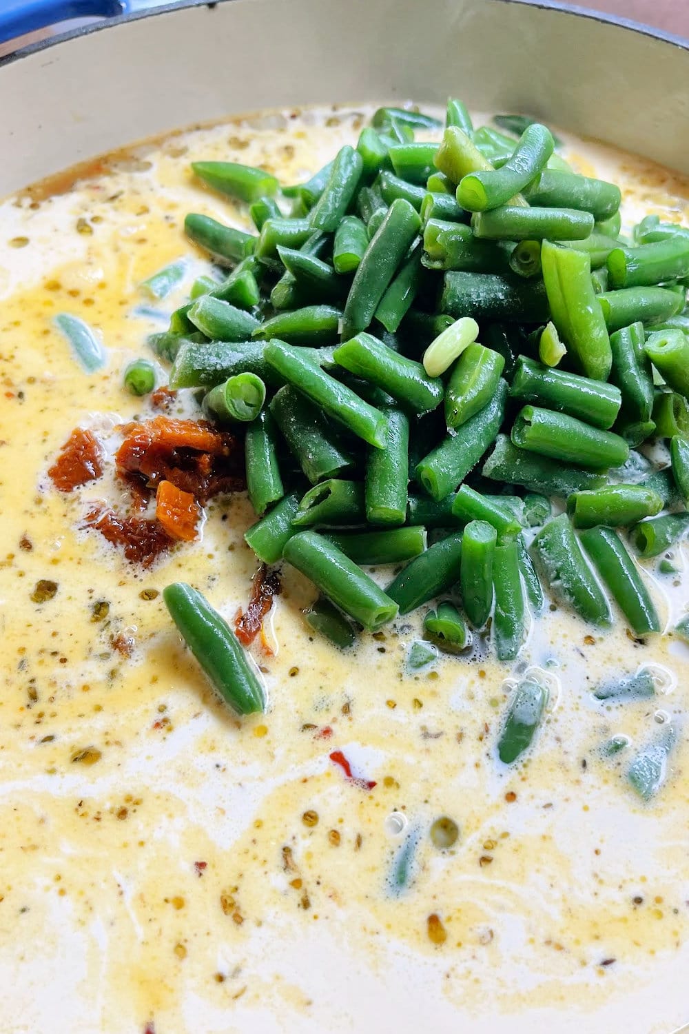 Cream, broth, sundried tomatoes, and green beans added to the skillet.