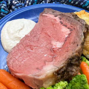 A nice thick slice of medium-rare prime rib on a plate with horseradish sauce.