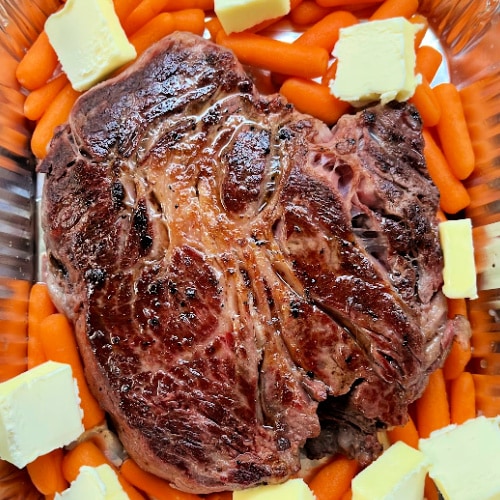 Pot roast in a pan with aromatics and butter, ready for the smoker.