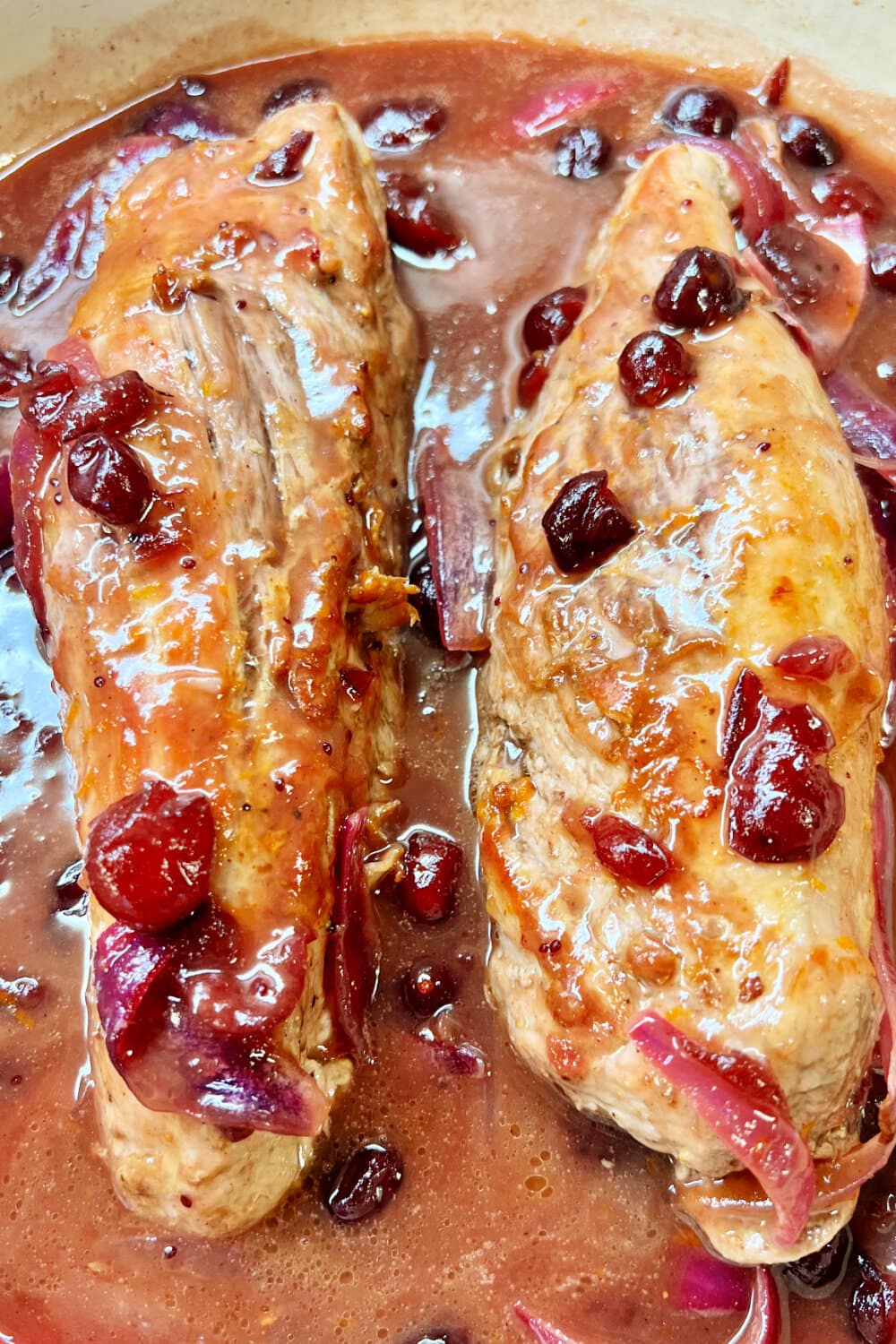 Two pork tenderloins nestled in cranberry sauce in a skillet. 