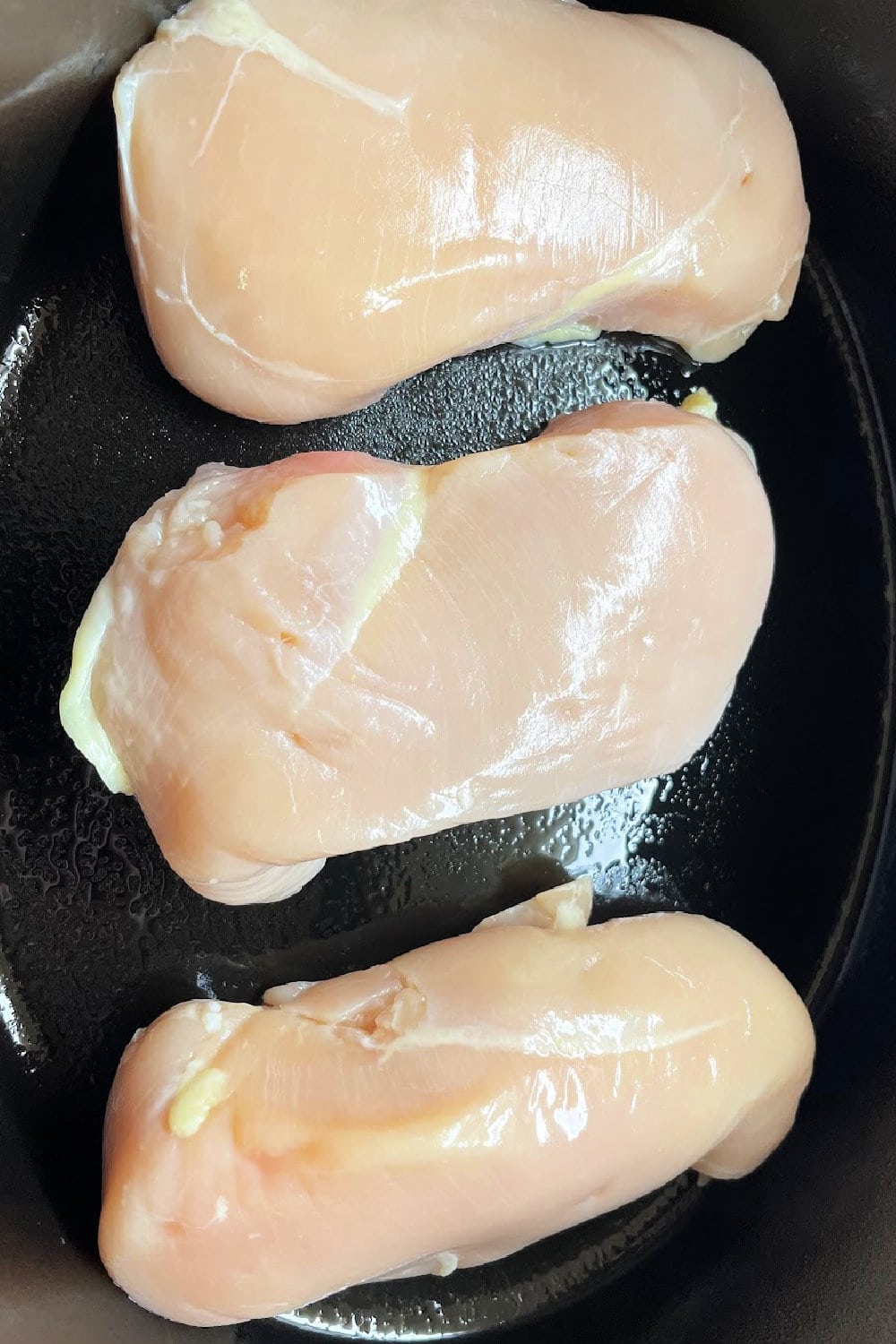Boneless, skinless chicken breasts placed across the bottom of a slow cooker. 