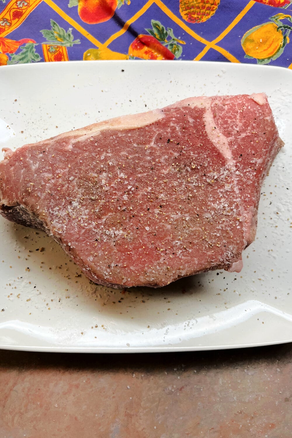 Rump roast resting on a white plate, ready to be rubbed with butter.