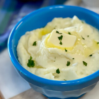 Butter mashed potatoes with parsley in a blue serving bowl.