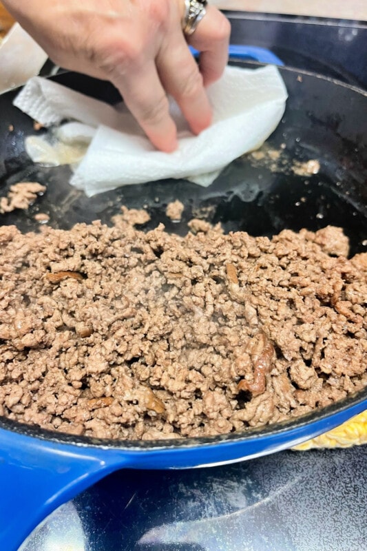 Removing fats from a skillet of ground beef. 