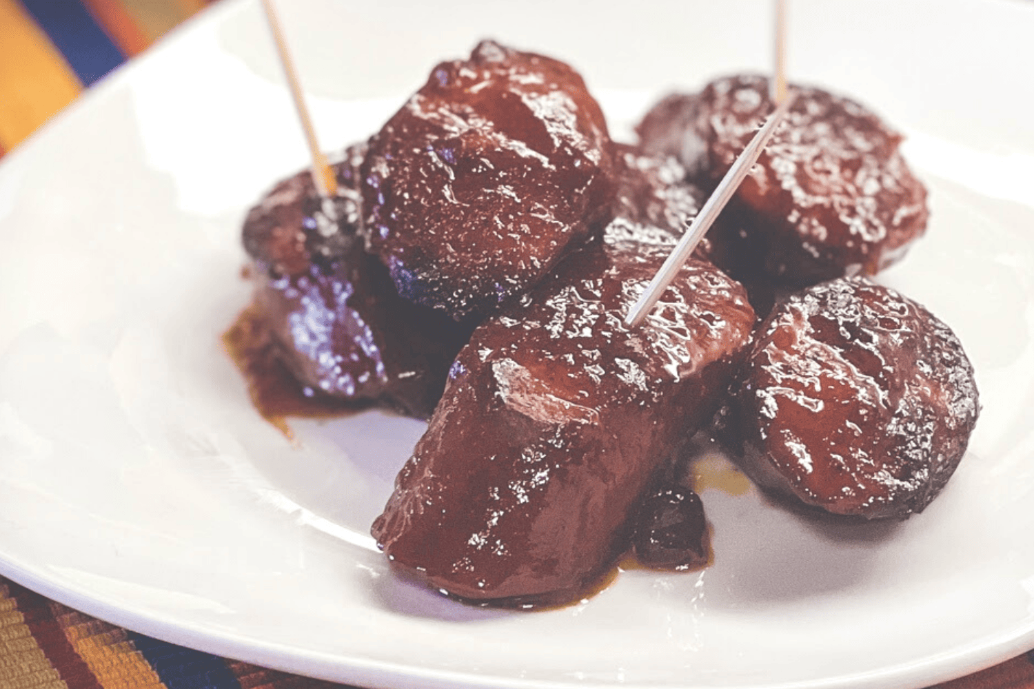 Big game sweet and spicy kielbasa sausage bites on a white plate with toothpicks. 