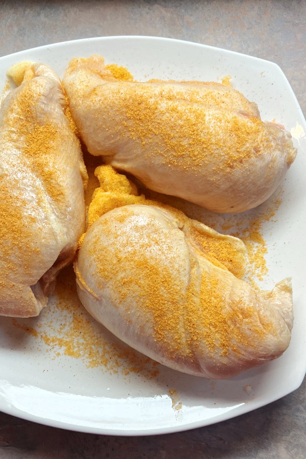 Three boneless, skinless chicken breasts with seasoned salt on top. 