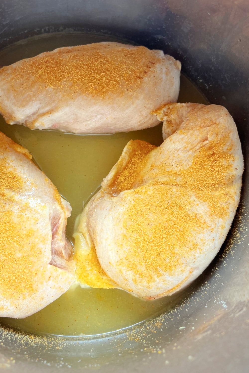 Three seasoned chicken breasts placed into broth in the Instant Pot. 