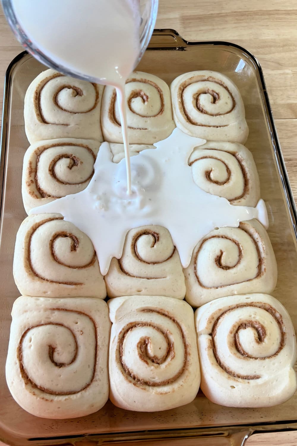 Pouring heavy cream over raised cinnamon rolls. 