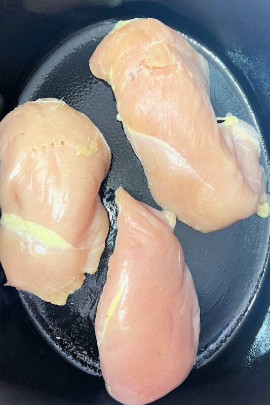 Chicken breasts placed into a greased slow cooker. 