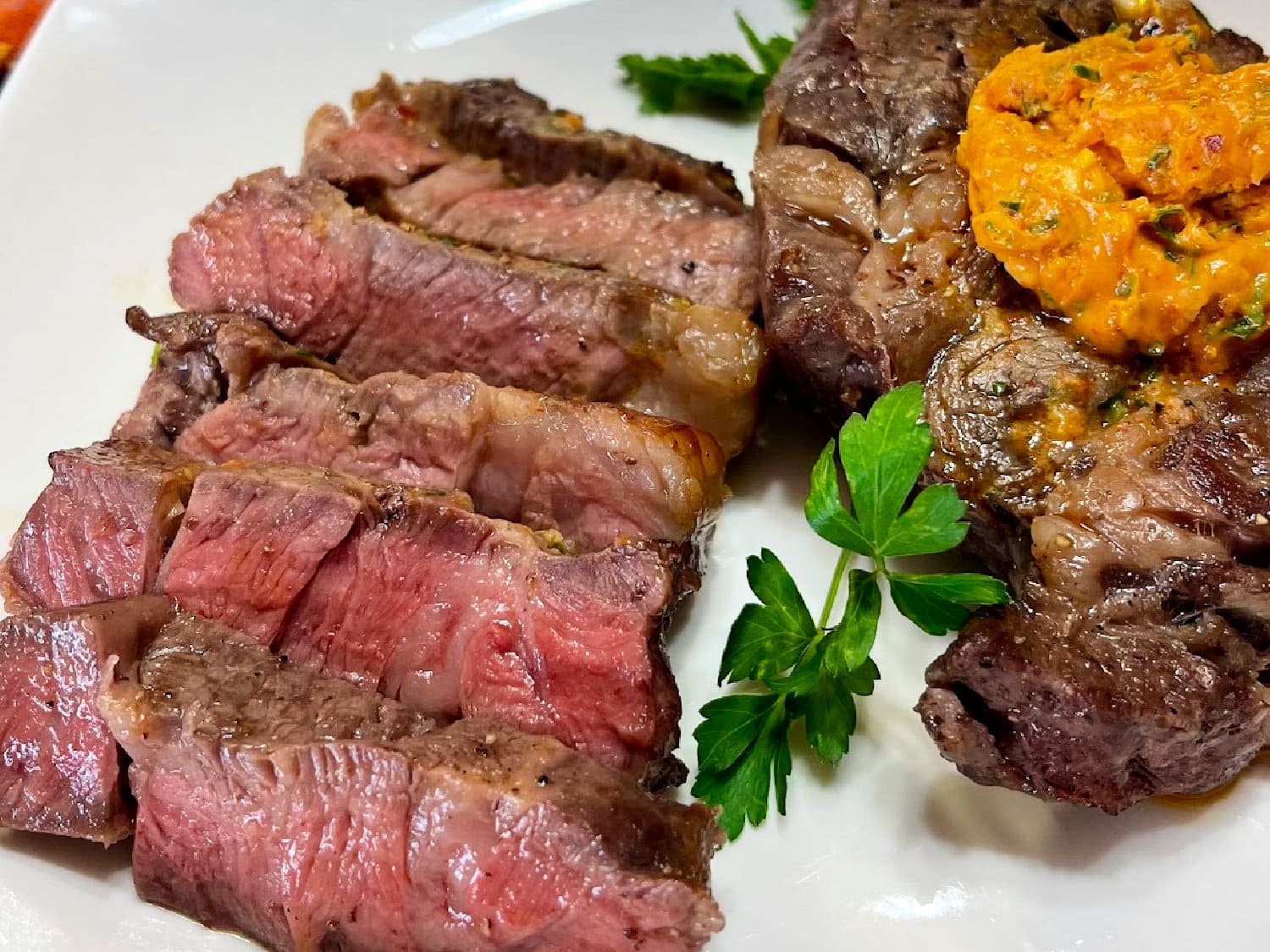 Sliced chuck eye steak shingled on a white plate. 