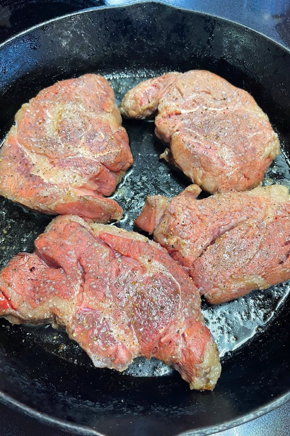 Four chuck eye steaks placed into a cast iron skillet. 