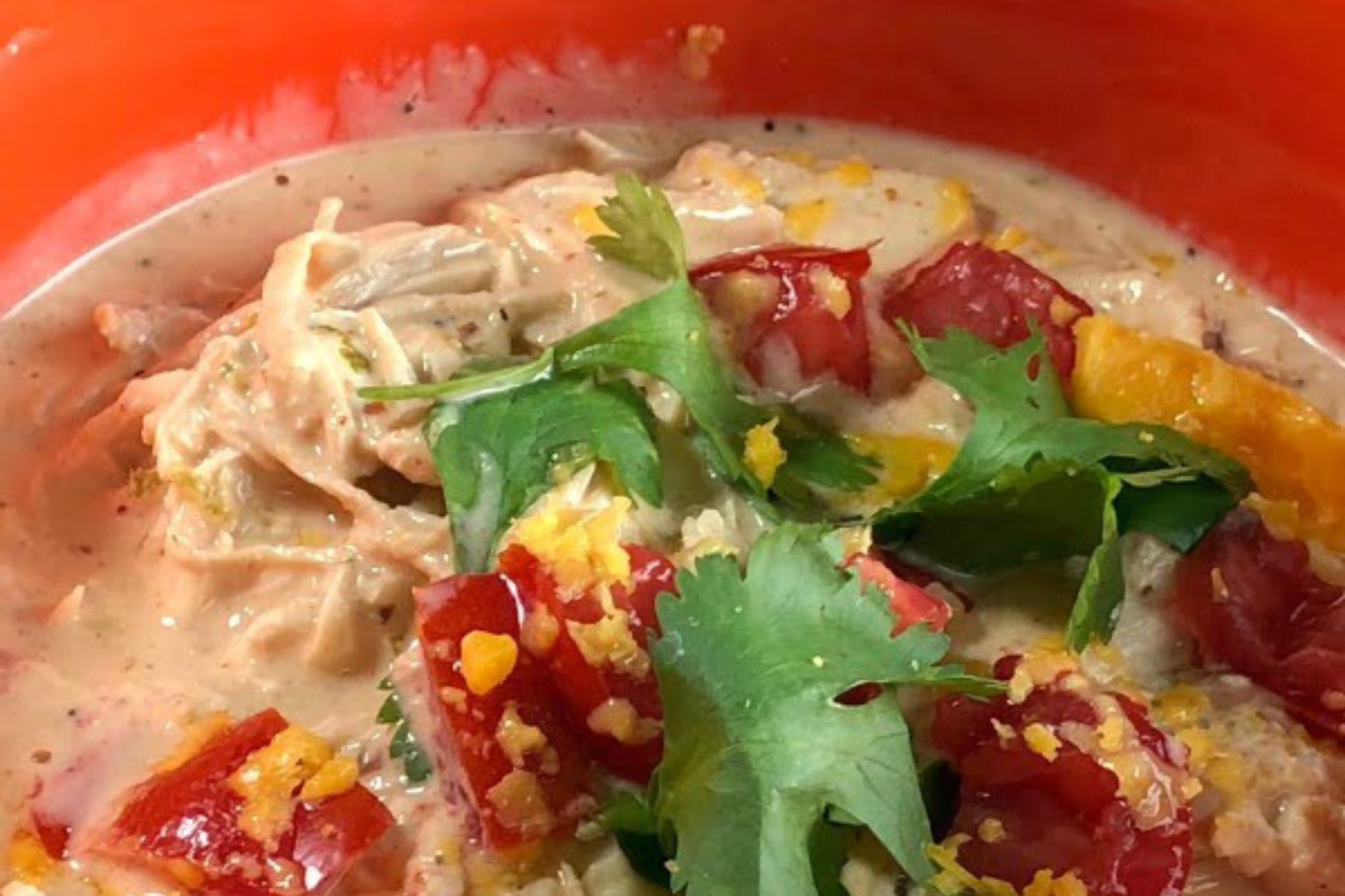Creamy Fiesta Chicken Soup in a red bowl with tomatoes and garnish. 