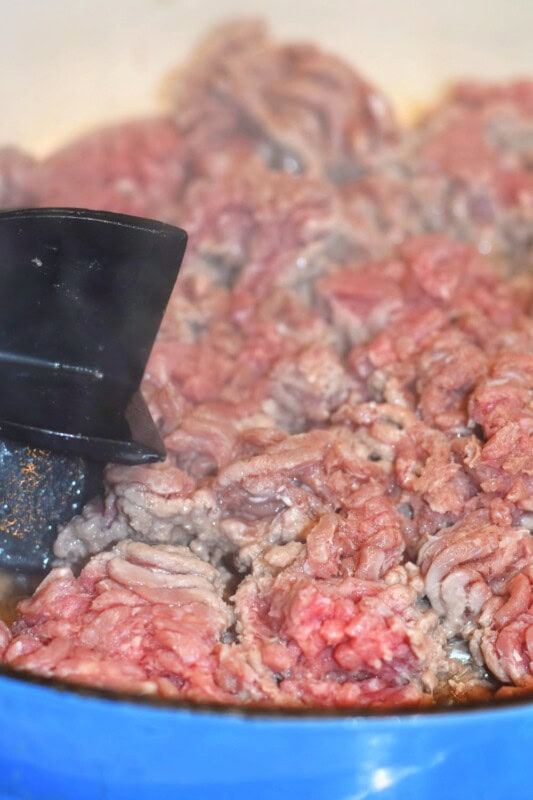 Crumbled ground beef cooking in a blue skillet. 