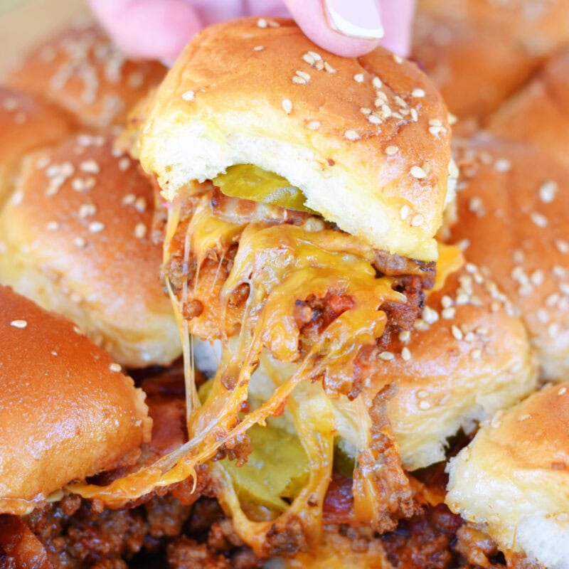 Lifting a cheeseburger slider on a hawaiian roll out of the baking pan.