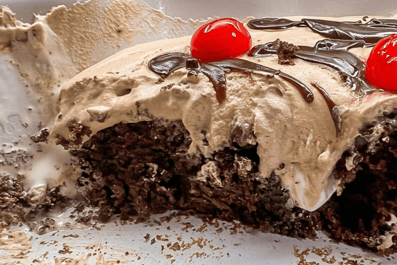 Hot Chocolate Poke Cake with fudge in a cake pan with cherries. 