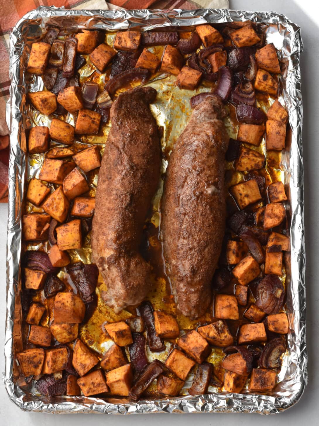 Pork Tenderloin Sheet Pan Dinner on a foil sheet pan with sweet potatoes and red onions. 
