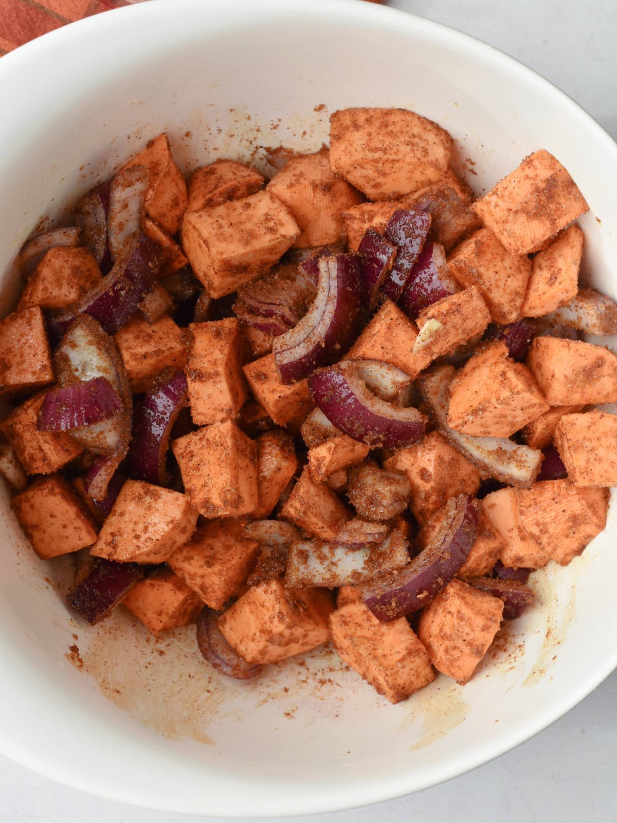 Seasoned potatoes and red onions in a mixing bowl. 