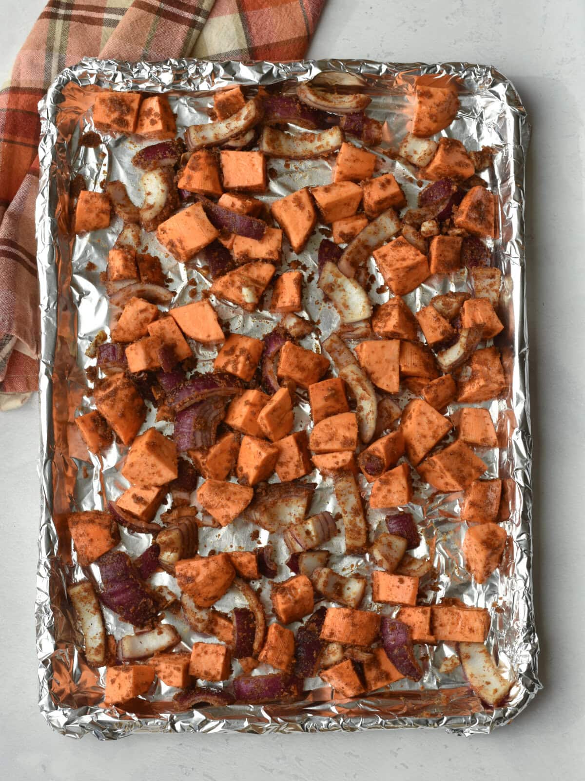 A foil wrapped sheet pan with partially cooked seasoned sweet potatoes and red onions. 