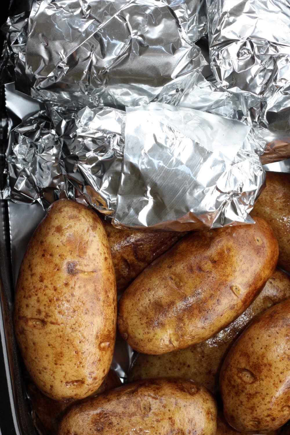 Foil-wrapped potatoes and naked potatoes in a roaster oven. 