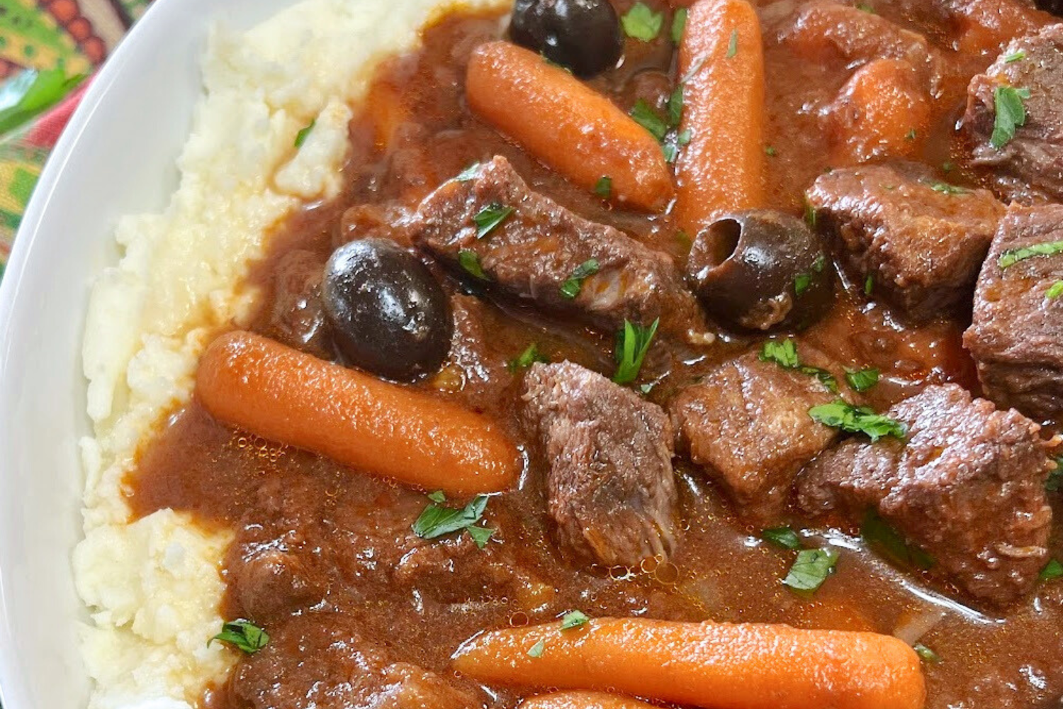 Beef stew with olives and carrots over mashed potatoes in a bowl. 