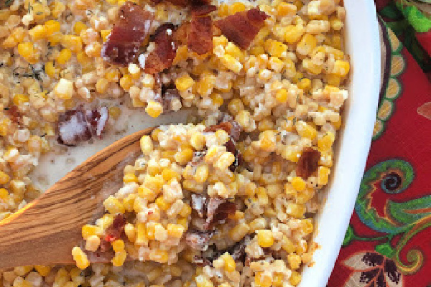 Creamed corn in a roasting pan with a spoon full of corn and bacon on top.