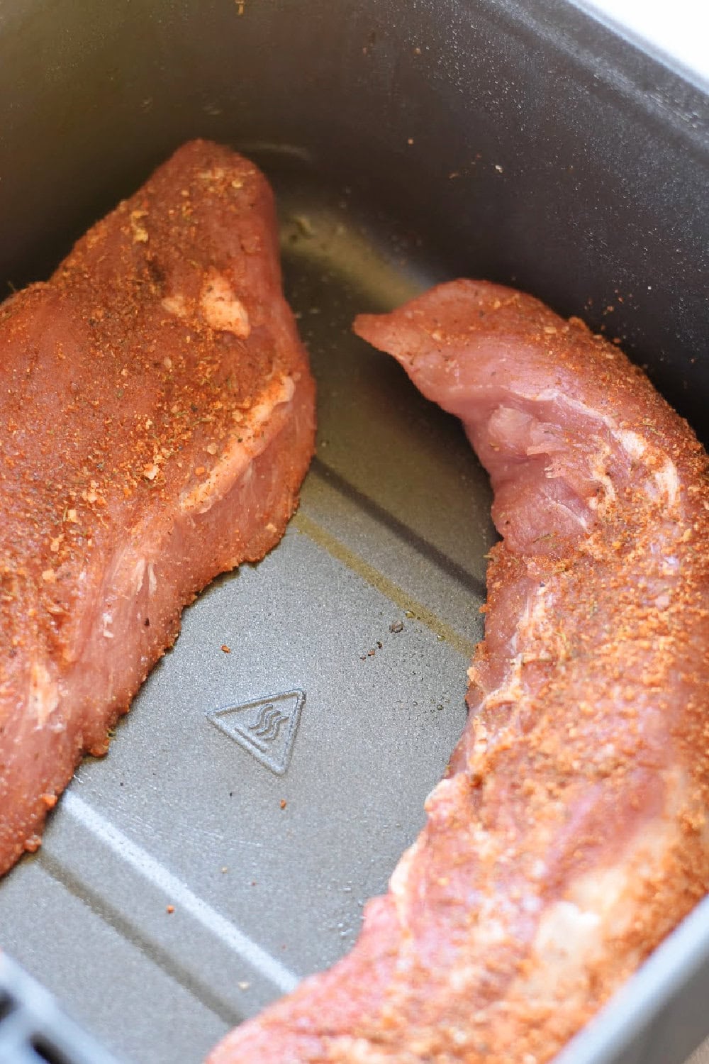 Seasoned pork tenderloins placed into the air fryer basket to cook. 