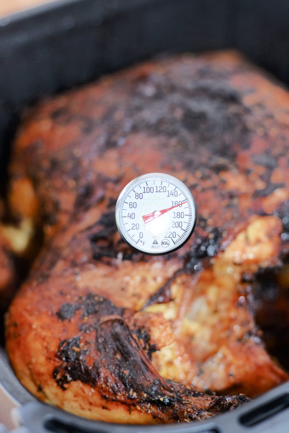 Air fryer chicken with an instant-read meat thermometer in the breast. 