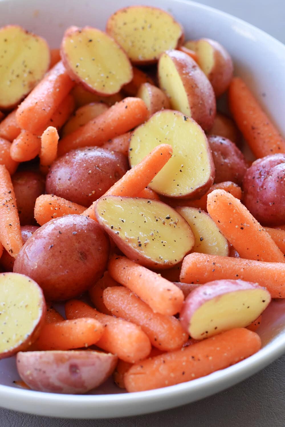 Baby carrots and potatoes drizzled with oil in a large mixing bowl. 