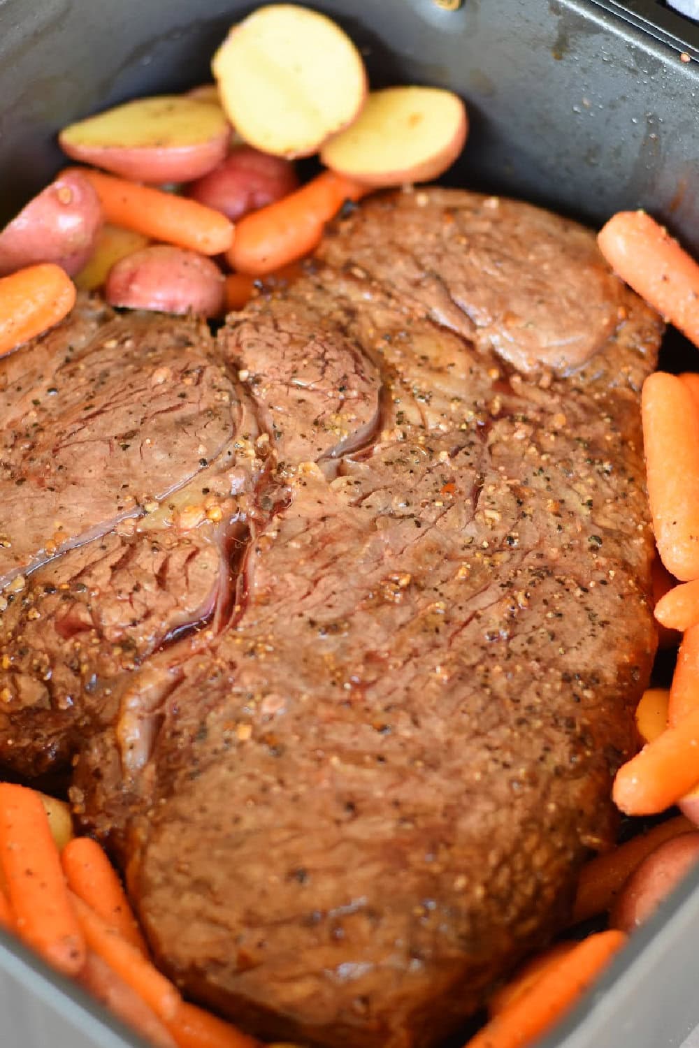 A chuck roast surrounded with baby carrots and small red potatoes. 