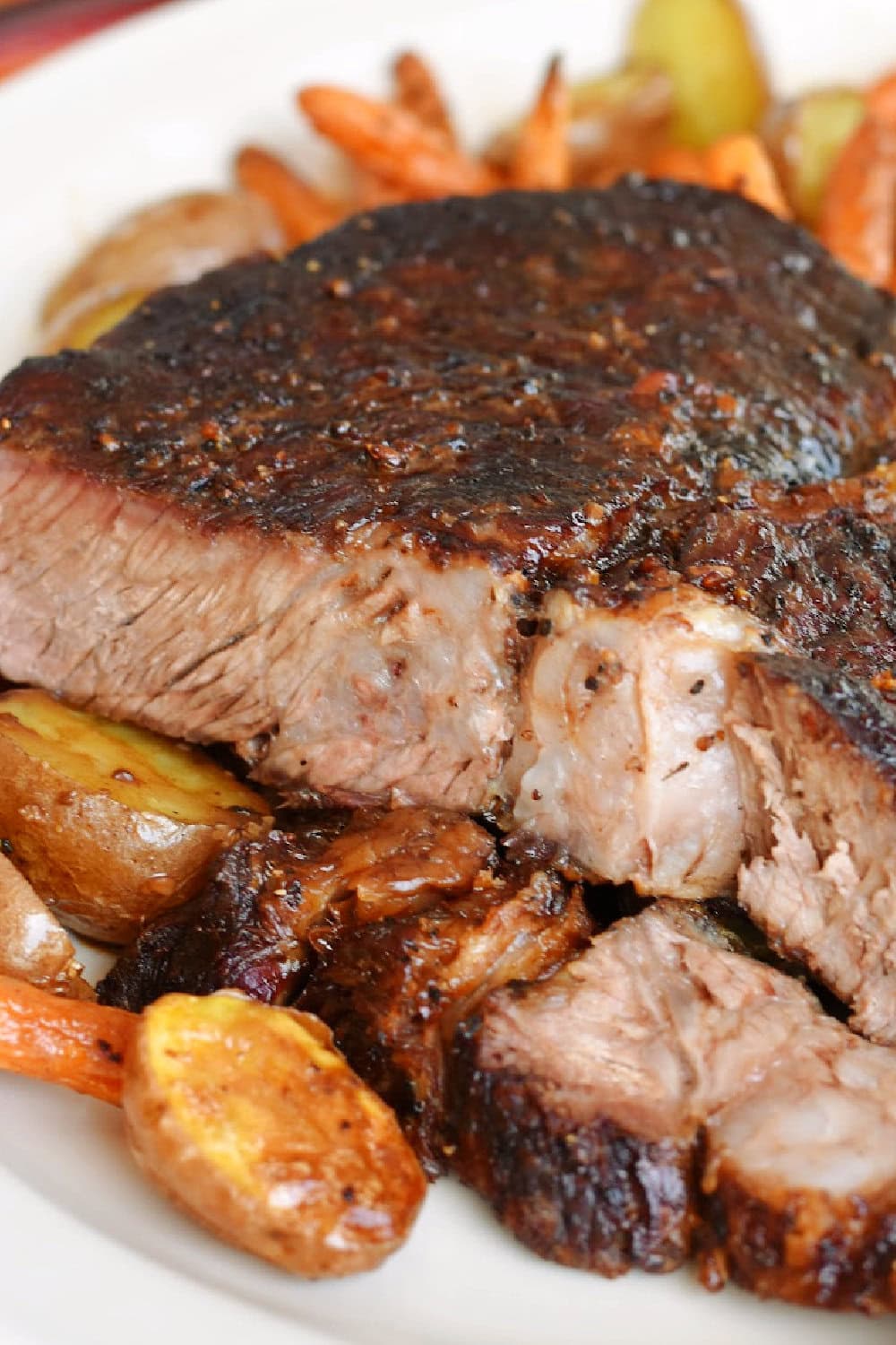 Side view of a sliced air fryer chuck roast with potatoes and baby carrots. 