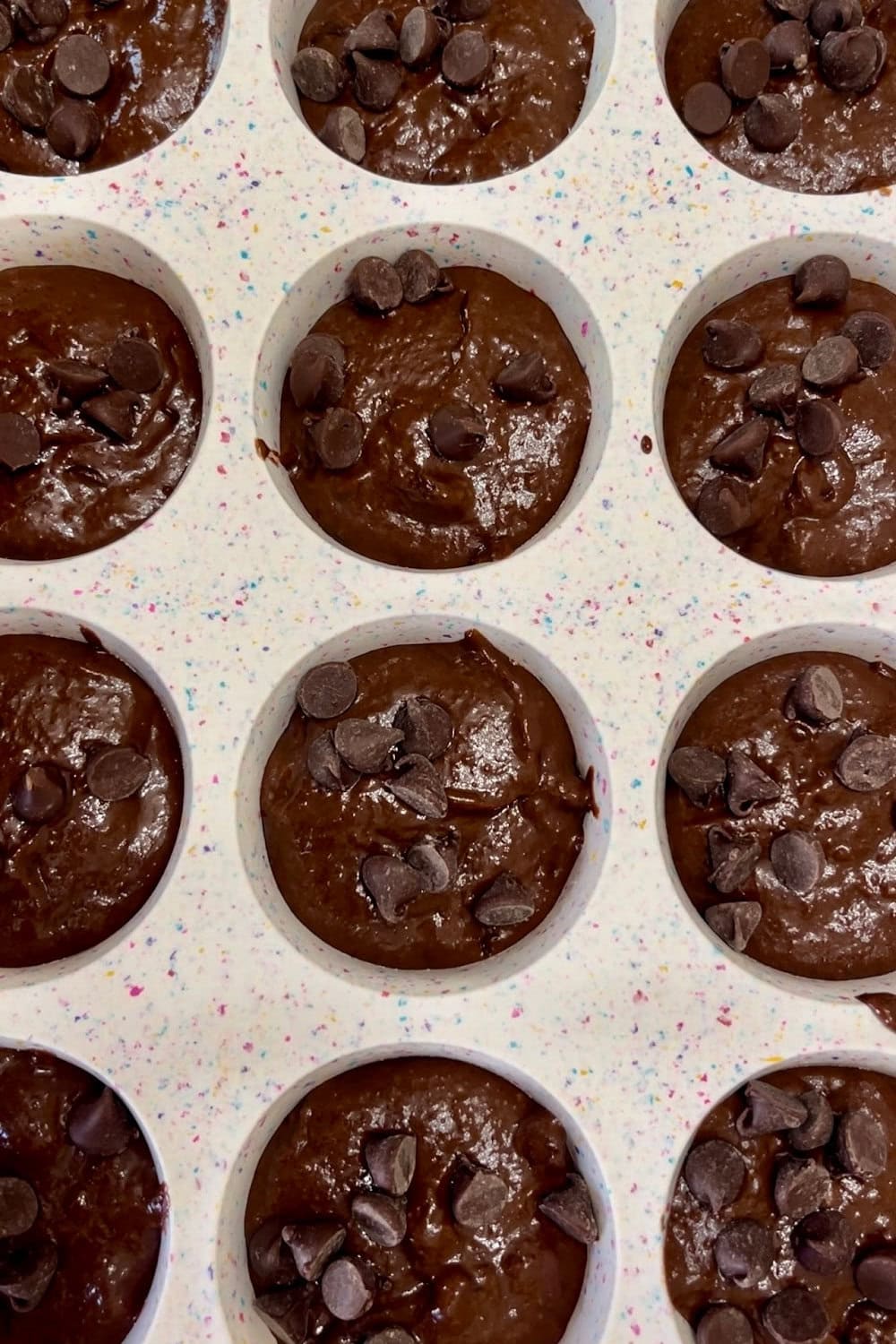 Unbaked chocolate muffin mix with applesauce in muffin tin. 