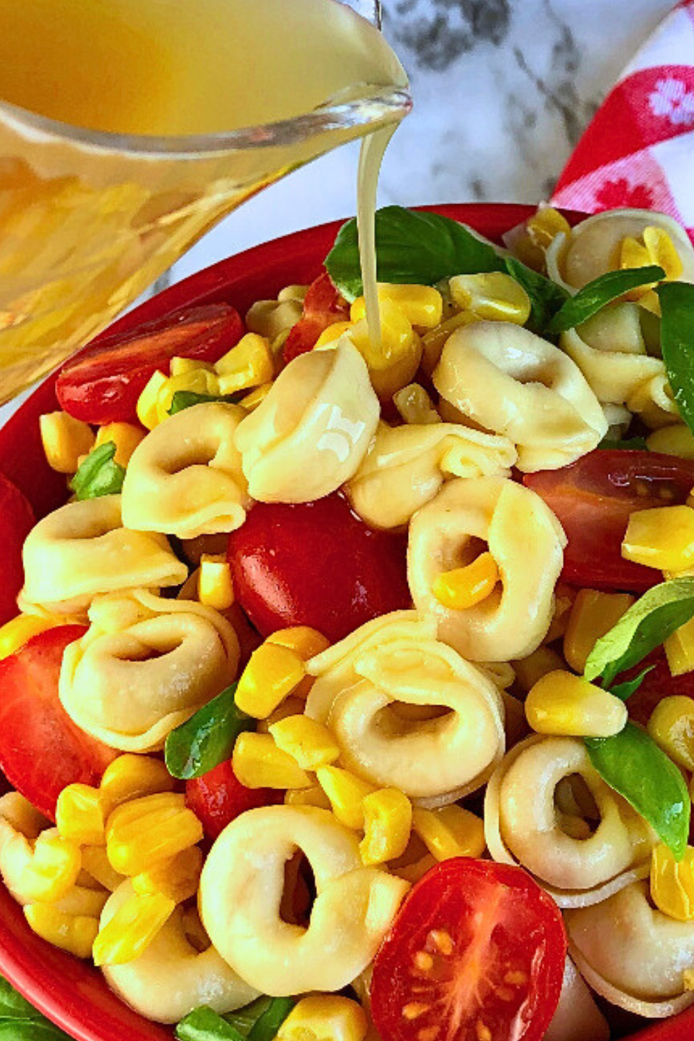 Cheese tortellini with corn and tomatoes in a summer salad with vinaigrette dressing being poured over it. 