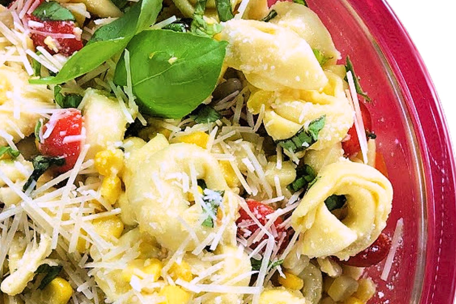 Tortellini pasta salad with tomatoes, corn, basil and a light vinaigrette dressing in a red bowl with parmesan cheese over it. 