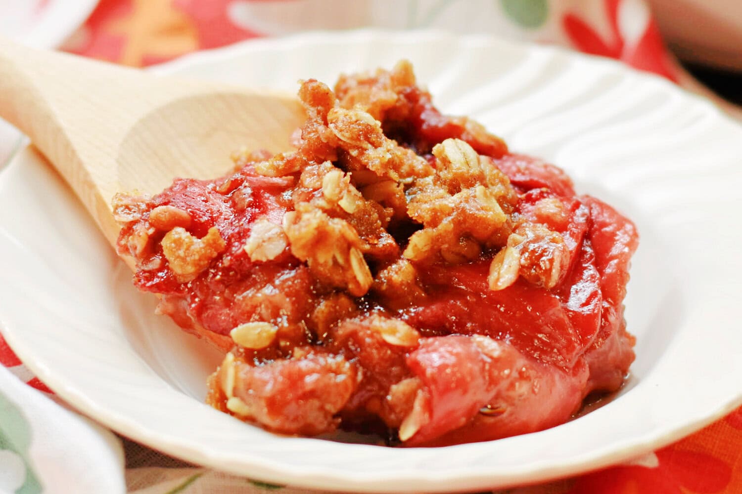 A large serving of Strawberry Crumble being placed into a white bowl. 