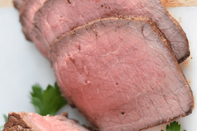 Beautiful medium-rare slices of Top Round Roast on a white cutting board. 