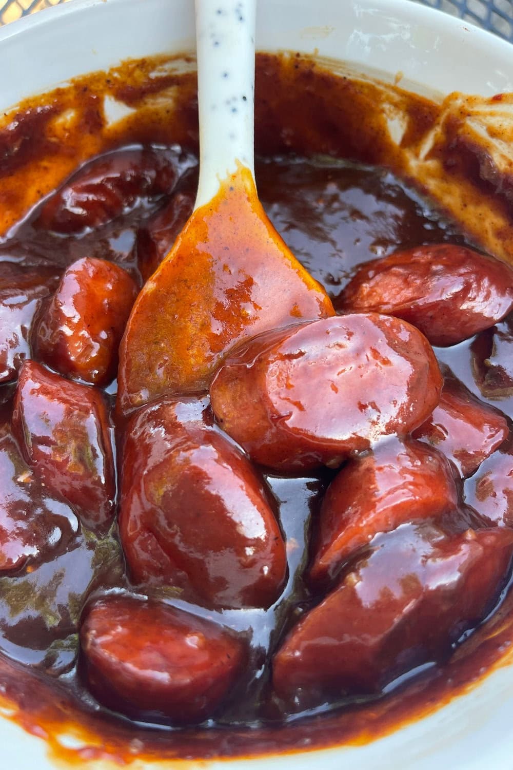 A delicious kielbasa appetizer with bbq sauce in a white bowl with a spoon. 