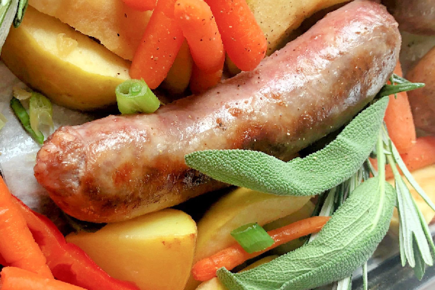 Pork sausage with potatoes, carrots, sage and rosemary in a sheet pan. 