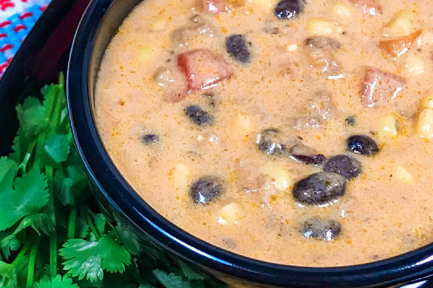 Creamy ground beef taco soup in a black bowl with garnish. 