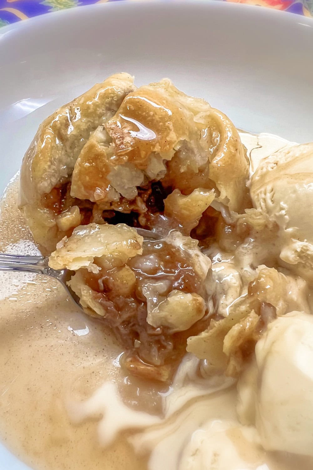 A spoon full of apple dumplings and ice cream. 